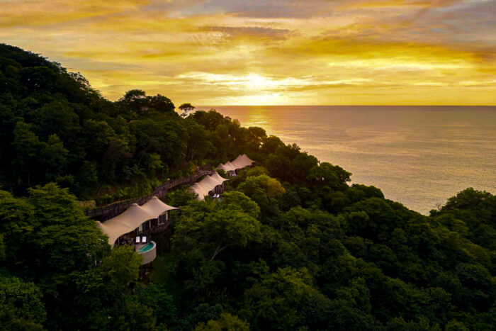 Luxury tented suites with private plunge pools perched on a forested hillside overlooking the ocean at sunset.Luxury tented suites with private plunge pools perched on a forested hillside overlooking the ocean at sunset