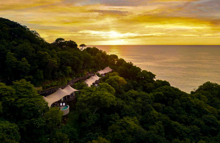 Luxury tented suites with private plunge pools perched on a forested hillside overlooking the ocean at sunset.Luxury tented suites with private plunge pools perched on a forested hillside overlooking the ocean at sunset